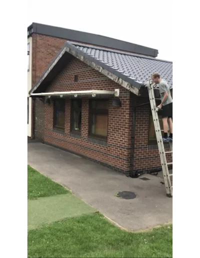 Man on ladder by brick building roof