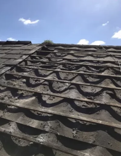 Damaged roof with missing shingles under blue sky.