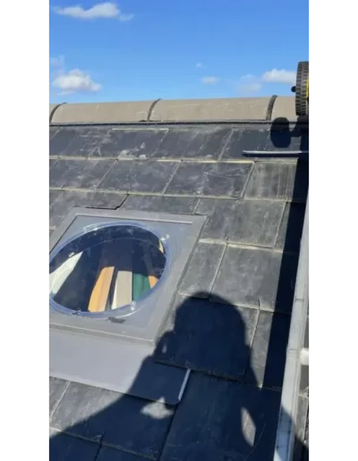 Circular skylight on slate roof with shadows.