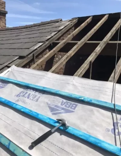 Roof repair with exposed beams and tarp covering.