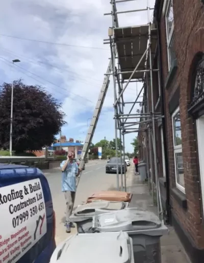 Man adjusts ladder next to building scaffolding.