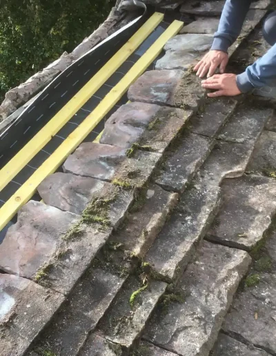 Repairing old mossy tile roof with hands.